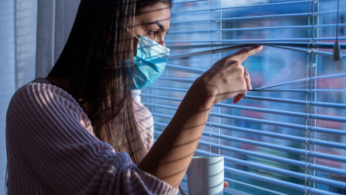 women in mask looking out window