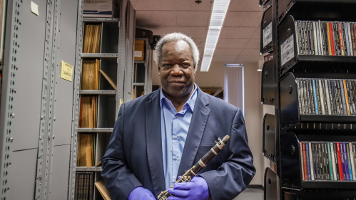 Archivist Vincent Pelote stands in the racks at the Institute of Jazz Studies holding a clarinet. 