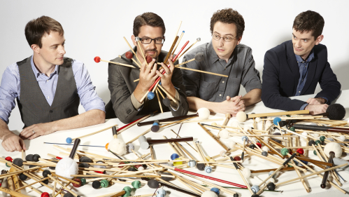 four men sitting at a table covered in musical mallets