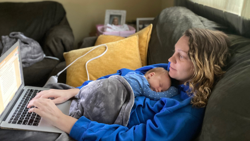 Cassie Botnick with her baby lying on her chest while she works on her laptop