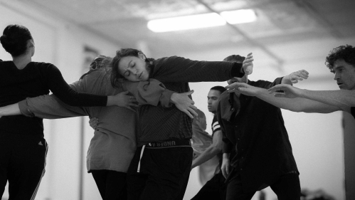 In a black and white photograph, dancers rehearse in a basketball court in New York.