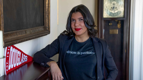 Cassandra “Cassie” Vega poses for a photo with her right arm resting on a fireplace in a Rutgers building.