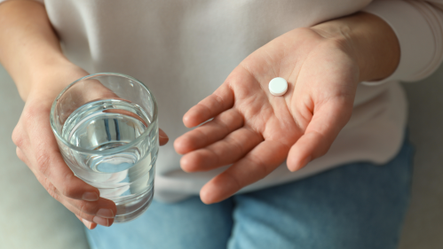 Woman holds pill and water glass