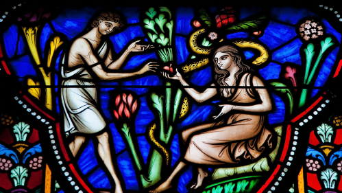 Adam and Eve eating the Forbidden Fruit in the Garden of Eden on a stained glass window in the cathedral of Brussels.