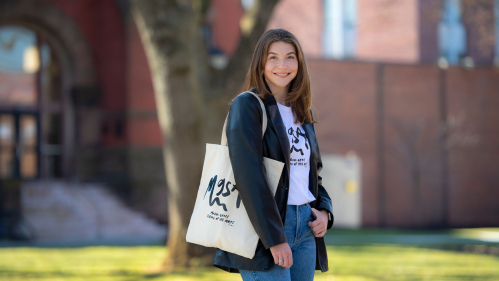 Emma Broggi wearing a t-shirt and holding a tote bag displaying artwork she designed 