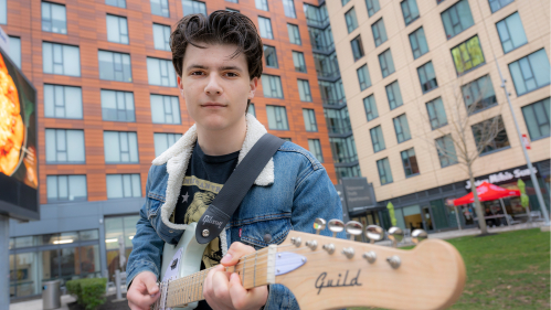 Jake Thistle holding his guitar standing at the Yard on College Ave