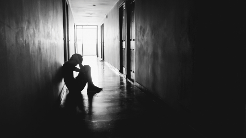 Depressed student sitting on floor of dark hallway