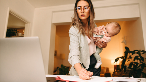 Mom holding baby while looking at a computer and taking notes 