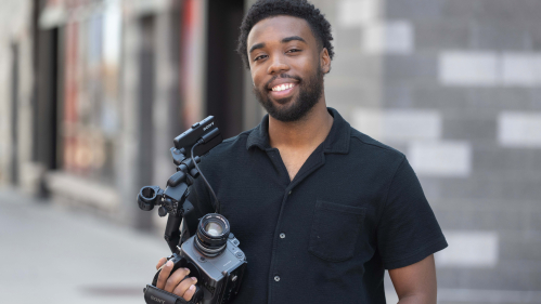 Terrance Leon George III standing in front of the Mason Gross building with his camera in his hand