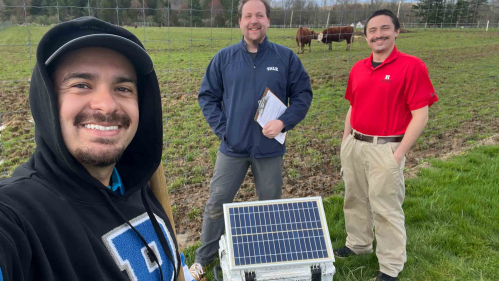 Three scientists stand in a field with a machine