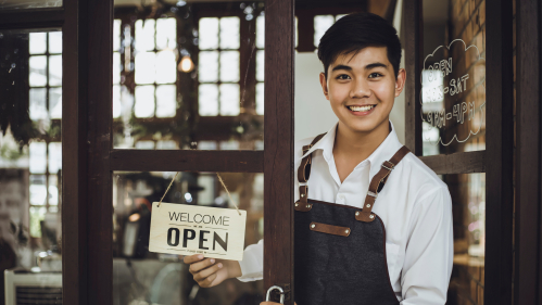 man turning a sign in a shop window to say 'open'