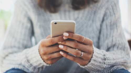 A young woman sitting on a couch texts on her smartphone.