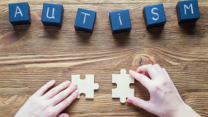 Blocks that spell "autism", hands on two puzzle pieces 