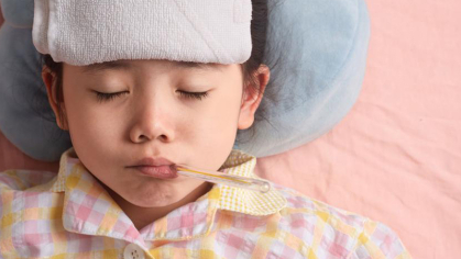 Image of a child lying in bed with a thermometer in their mouth and a towel on their forehead