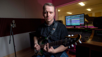 Doctoral student Aaron Vaders-Collins stares ahead, playing he guitar
