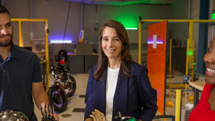 Rutgers School of Engineering professor Kristin Dana smiles at camera while standing in a robotics lab flanked by her students. 