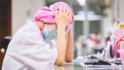 Nurse under stress sitting at desk hands on head 