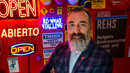 University Safety Officer Alejandro Ruiz stands in front of a wall of neon signs in his office