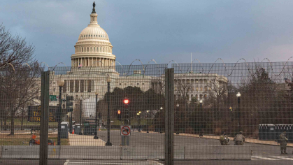 A view of the United States Capitol can be seen from behind a fence.