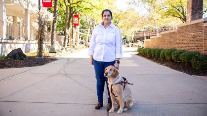 Nimit Kaur standing on a concrete walkway with her seeing-eye dog