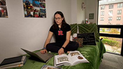Jacqueline Giz sitting on her bed with a green comforter in her dorm room