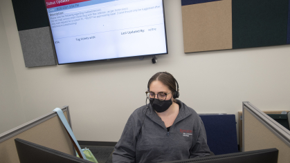 Student sitting at help desk computer with large screen in the background