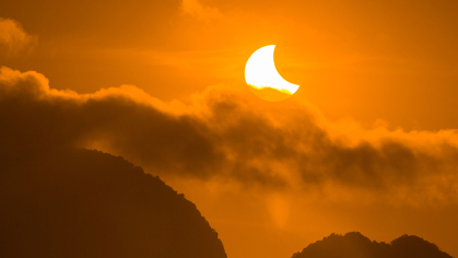Partial solar eclipse over clouds with an orange sky