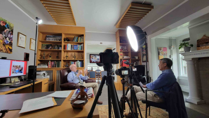 Two men in office, one interviewing the other with video camera