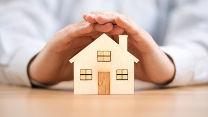 Small model house with hands covering it