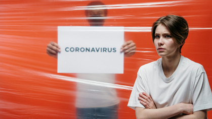 Women standing infront of orange background and a sign that says Coronavirus