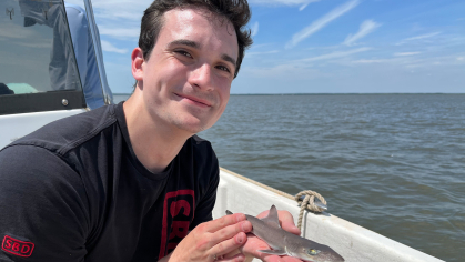 Salvatore Fricano on a boat with water in the background holding a fish