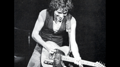 Bruce Springsteen playing the guitar against a black background