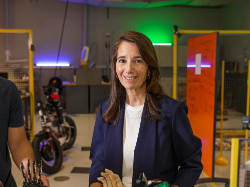 Rutgers School of Engineering professor Kristin Dana smiles at camera while standing in a robotics lab flanked by her students. 