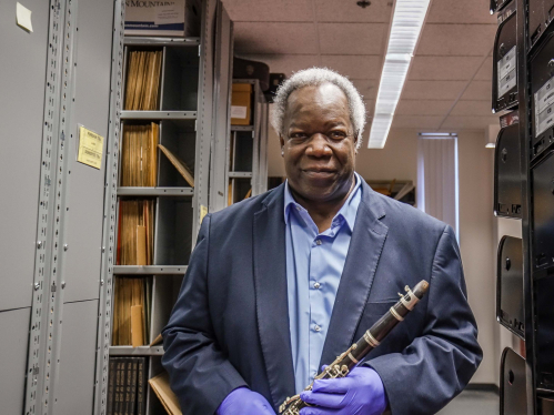Archivist Vincent Pelote stands in the racks at the Institute of Jazz Studies holding a clarinet.