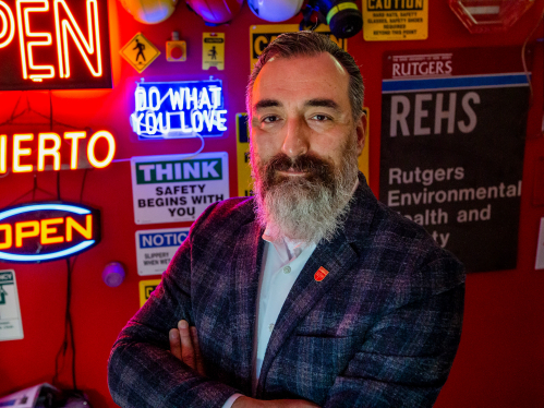 University Safety Officer Alejandro Ruiz stands in front of a wall of neon signs in his office