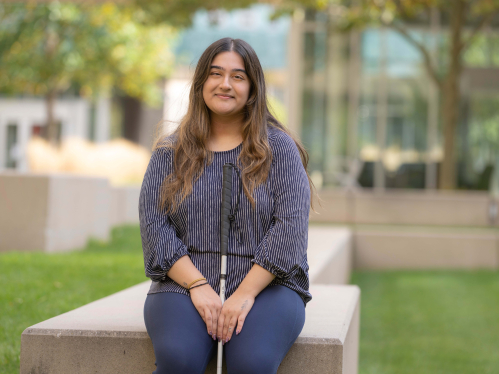 Vidhi Raval seated on campus with her guide stick