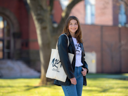Emma Broggi wearing a t-shirt and holding a tote bag displaying artwork she designed 