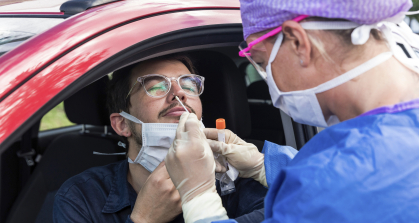 A health care worker at a drive-through testing center uses a nasal swab to test a patient for COVID-19