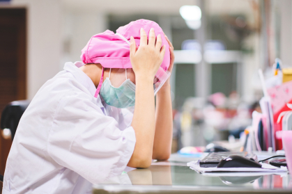 Nurse under stress sitting at desk hands on head 