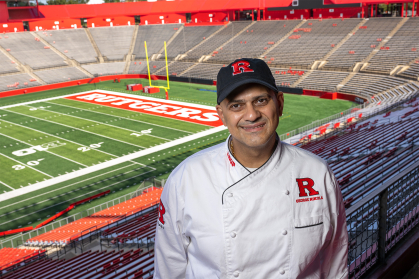 George Nikola wearing chef uniform with a view of the stadium behind him