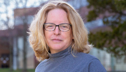 woman standing in front of brick building wearing a blue turtleneck