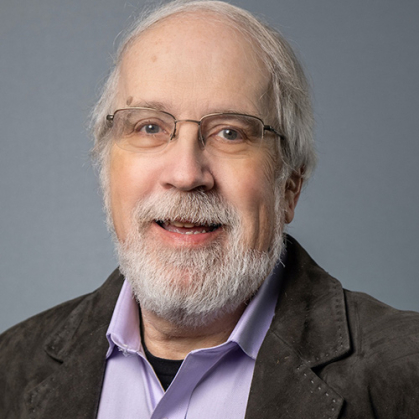 Man with grey jacket and lavender shirt against a gray background.