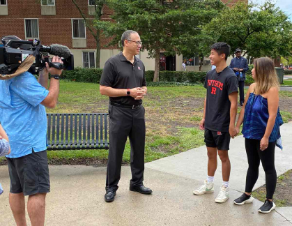 Rutgers President Jonathan Holloway chats with Ethan Thai and his mother, May, as an NBC camera crew captures the moment.