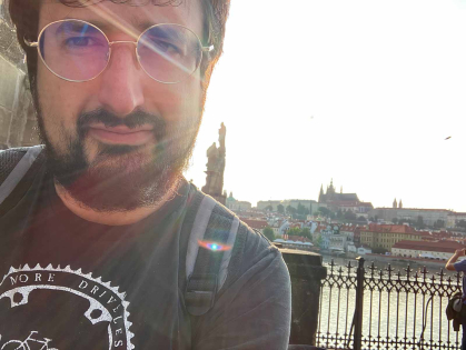 Ilya Slavutskiy stands near Charles Bridge. Behind him is a view of the Prague Castle complex and St. Vitus Cathedral.