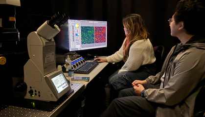 Two students sit before a computer screen in a darkened room