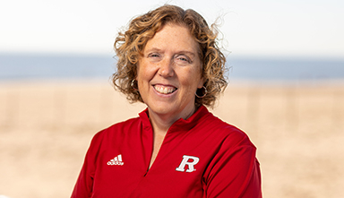 Woman wearing red sports zipper top with Rutgers logo stands on a beach