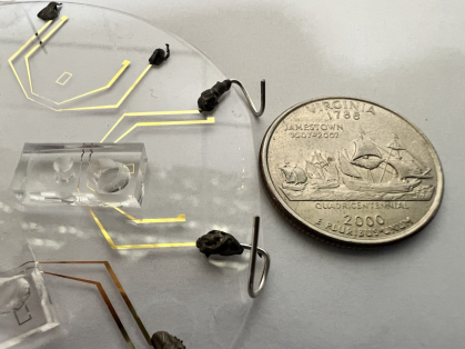 Clear plastic device with electrodes is placed next to a quarter and is slightly bigger