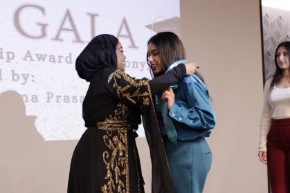 AACC senior program coordinaor Shaheena Shahid putting a stole on a graduate on stage