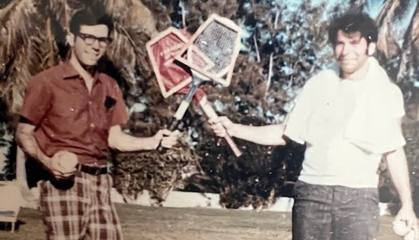 Two smiling young men holding tennis rackets in an outdoor setting