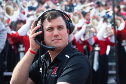 Chris Keri wearing a headset with Rutgers Marching Band in the Background